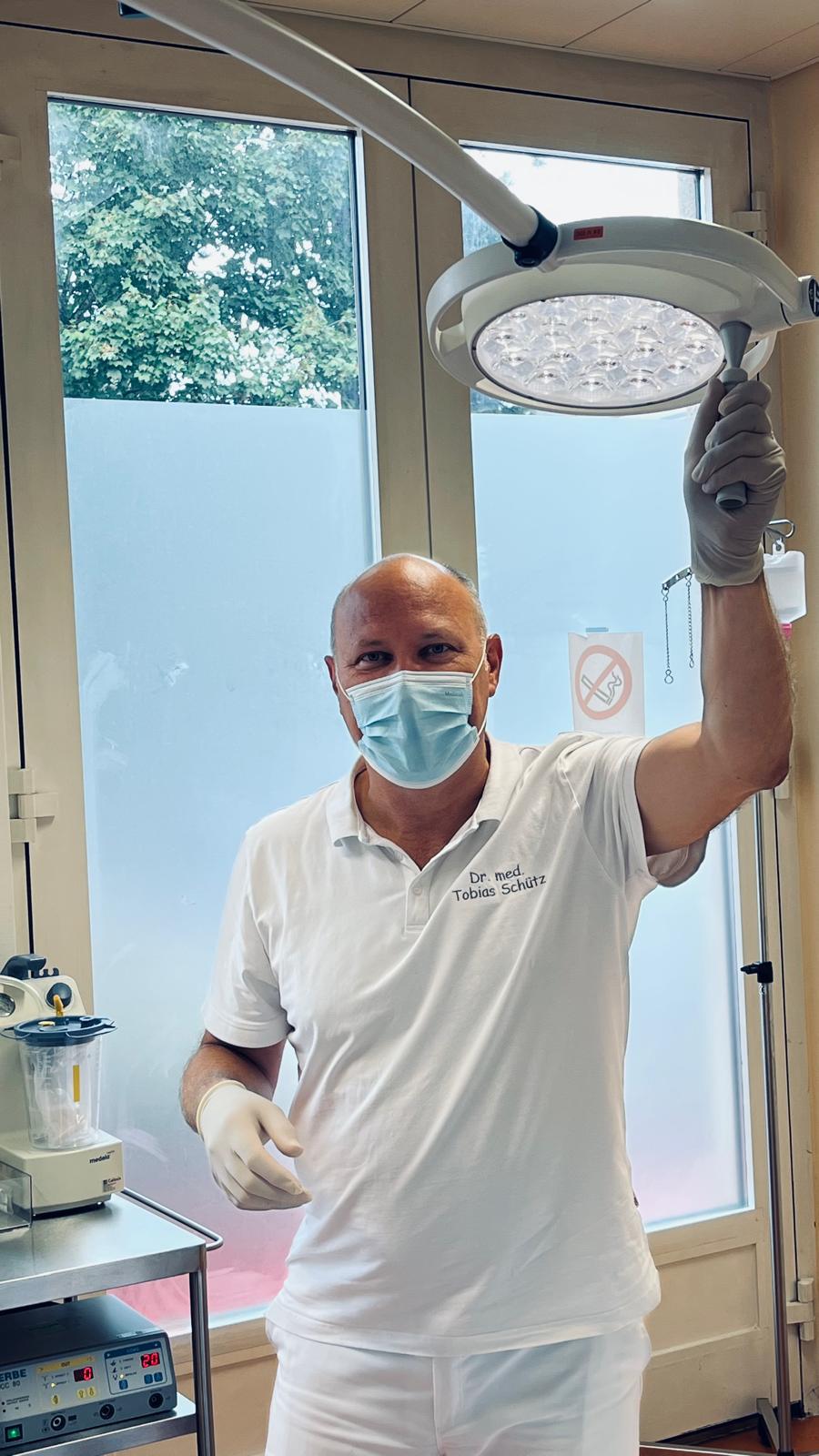 Dr. med. Tobias Schütz im Operationsraum der Praxis, er richtet die Operationsleuchte aus